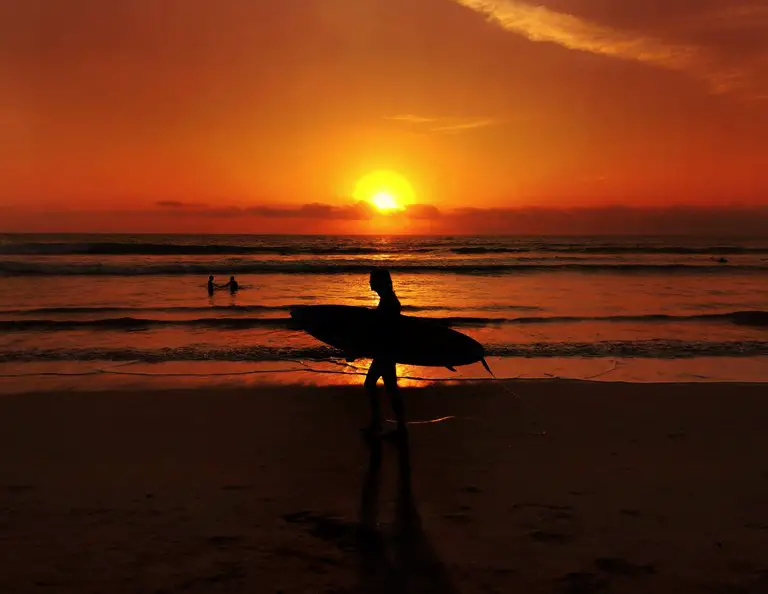Hombre con tabla de surf con el atardecer de fondo en la regencia de Badung, Bali