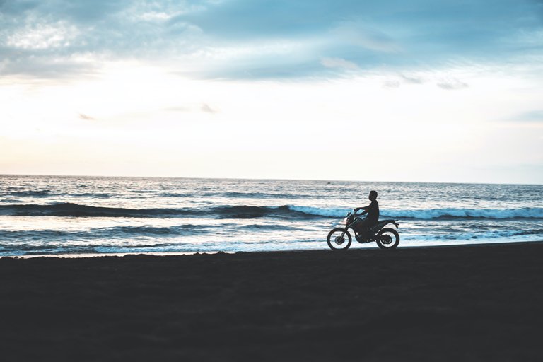 Hombre pasando en moto por la playa de Pigstone, Bali